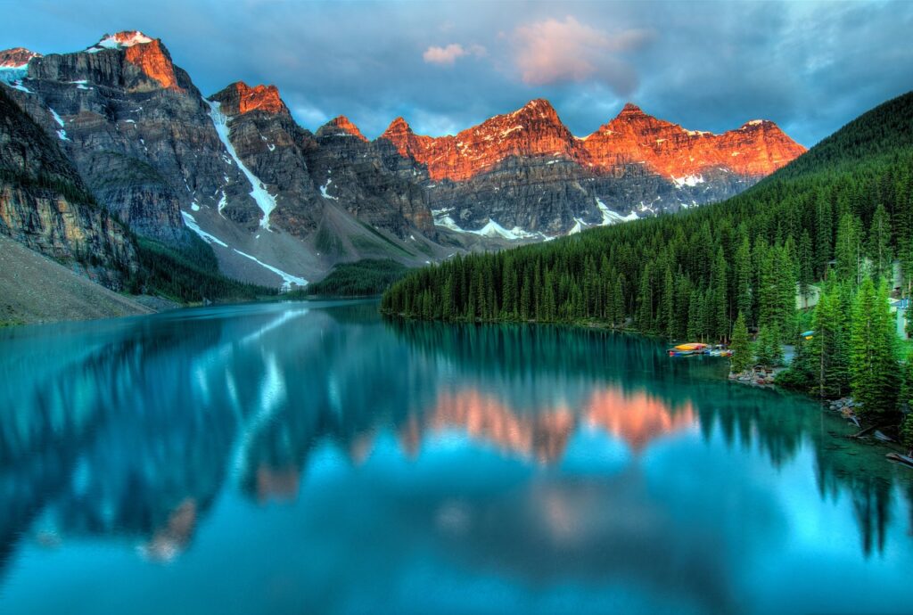 Ein unberührter, klarer Bergsee, der die majestätischen Gipfel bei Sonnenaufgang spiegelt, als Symbol für reines und natürliches Wasser.