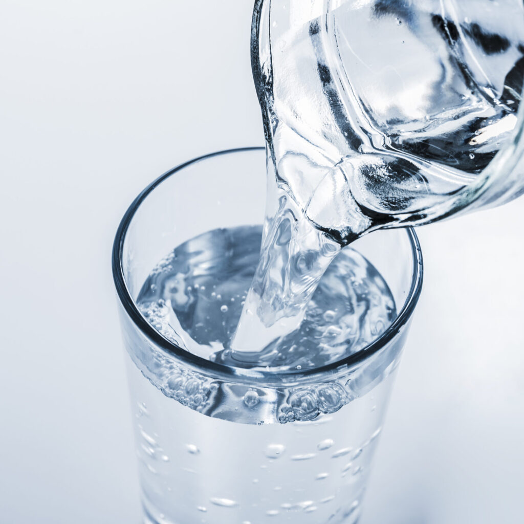 Klares, gefiltertes Wasser wird aus einer Glaskaraffe in ein Trinkglas gegossen.