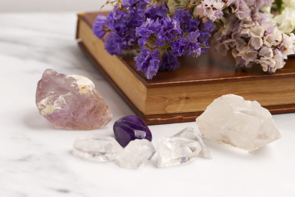 Eine Auswahl von Amethyst- und Bergkristallen, arrangiert mit getrockneten Blumen auf einem Buch mit Ledereinband, auf einer weißen Marmoroberfläche.