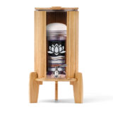 Ein Glas-Wasserfilter mit mehrstufiger Filterkartusche und Edelsteinen, eingefasst in einen Ständer mit Lichtschutz und Deckel aus hellem Bambus.