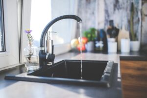 Klares Wasser fließt aus einem modernen Wasserhahn in ein Spülbecken, Symbol für sauberes Trinkwasser.