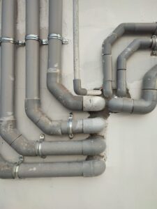 Komplexes System aus alten, grauen Wasserleitungen, die an einer Wand montiert sind.