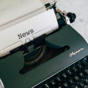 Eine klassische, grüne Schreibmaschine, in die ein Blatt Papier mit dem Wort 'News' eingespannt ist.