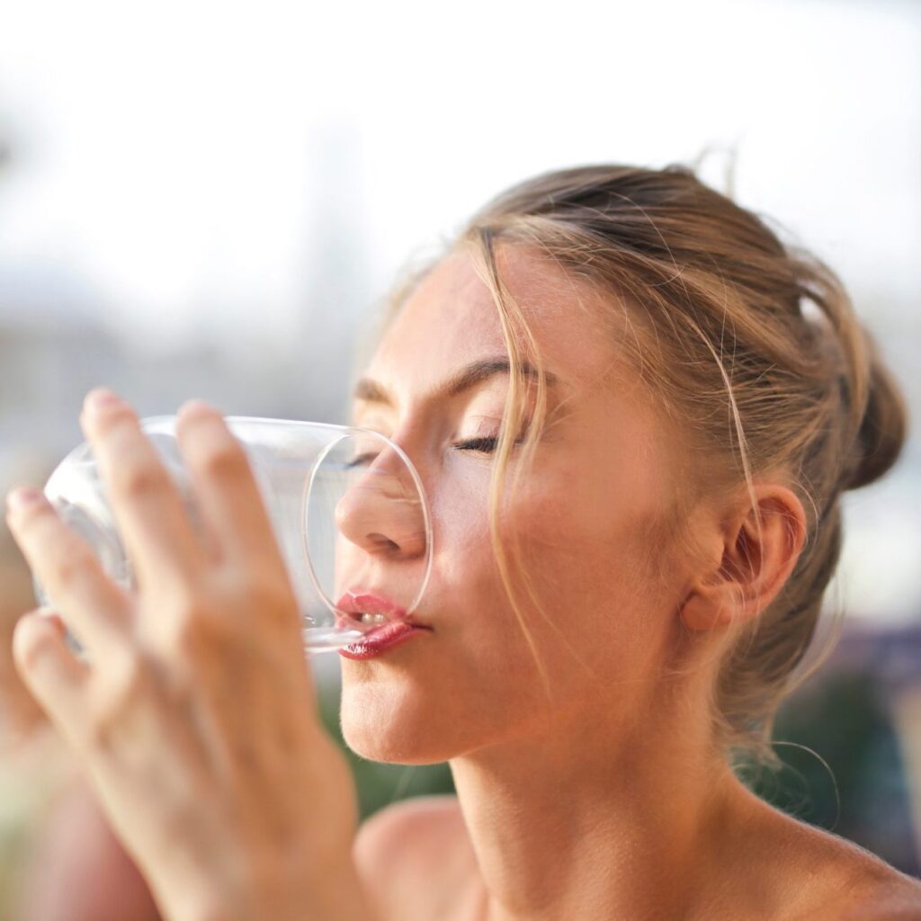 Eine junge Frau genießt mit geschlossenen Augen ein Glas reines, klares Wasser.