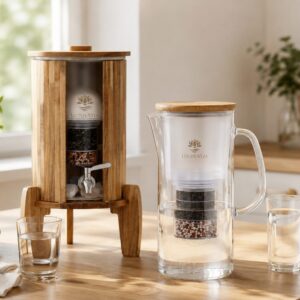 Ein hölzerner Wasserspender und eine gläserne Filterkaraffe für Trinkwasser stehen auf einer hellen Küchentheke.