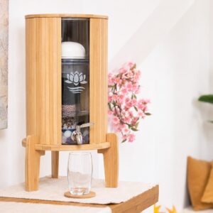Ein eleganter Wasserfilter aus Bambus mit einem Glasbehälter und Zapfhahn, aufgestellt in einem harmonisch eingerichteten Raum.