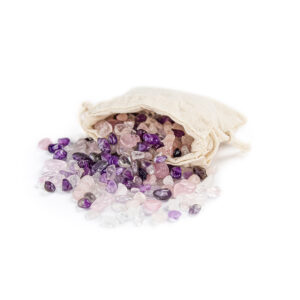 Eine Mischung aus violetten, rosa und durchsichtigen Edelsteinen, die aus einem kleinen Stoffbeutel auf eine weiße Oberfläche geschüttet wird.